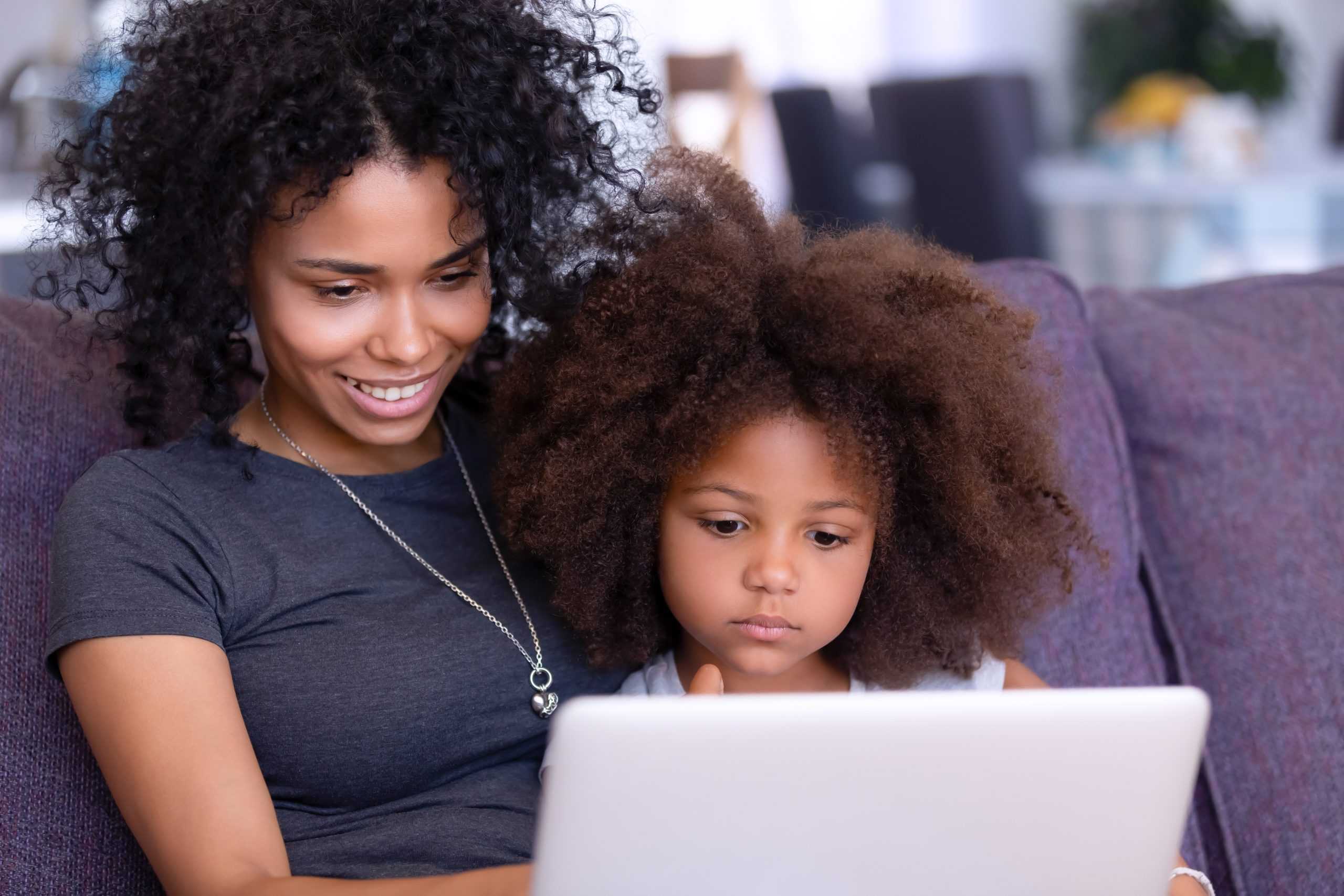 A mother and her ***** daughter sitting on a sofa looking at a computer.